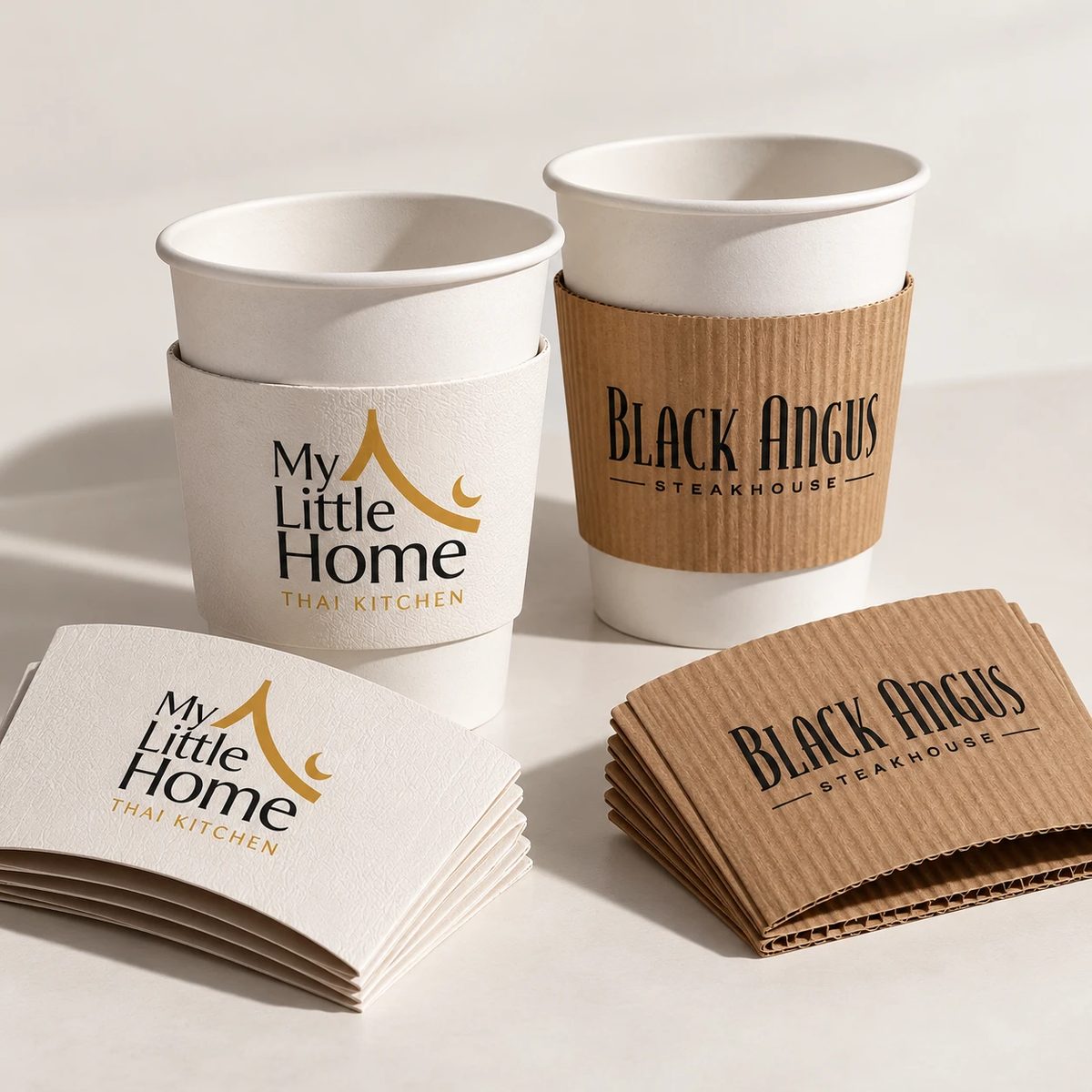 Custom coffee sleeves on paper cups: white embossed sleeve for My Little Home Thai Kitchen and kraft corrugated sleeve for Black Angus Steakhouse, with stacks of flat sleeves in front